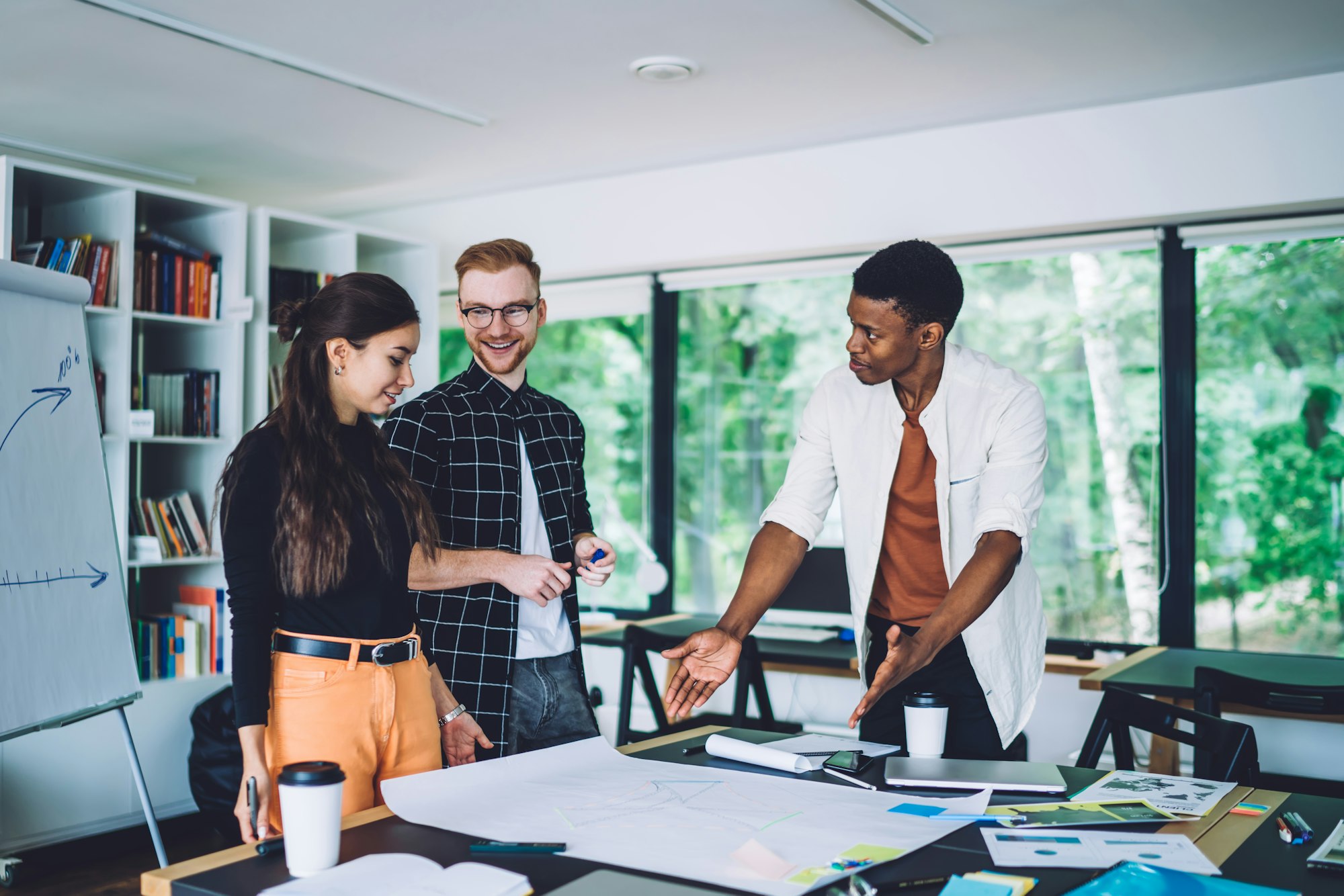 Cheerful adult multiethnic colleagues examining information in blueprint in modern office